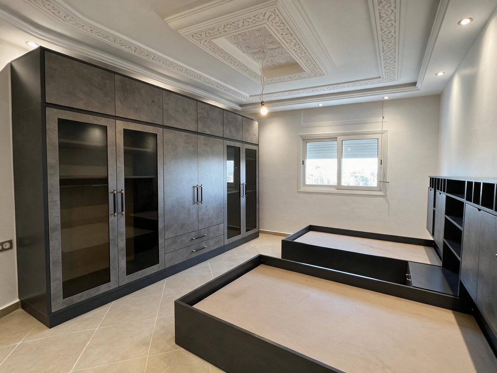 Dark wardrobe wall with glass doors and two beds under a decorated ceiling