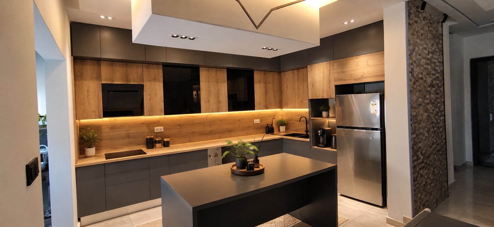 Kitchen in dark grey and wood with a central island and a stainless steel fridge